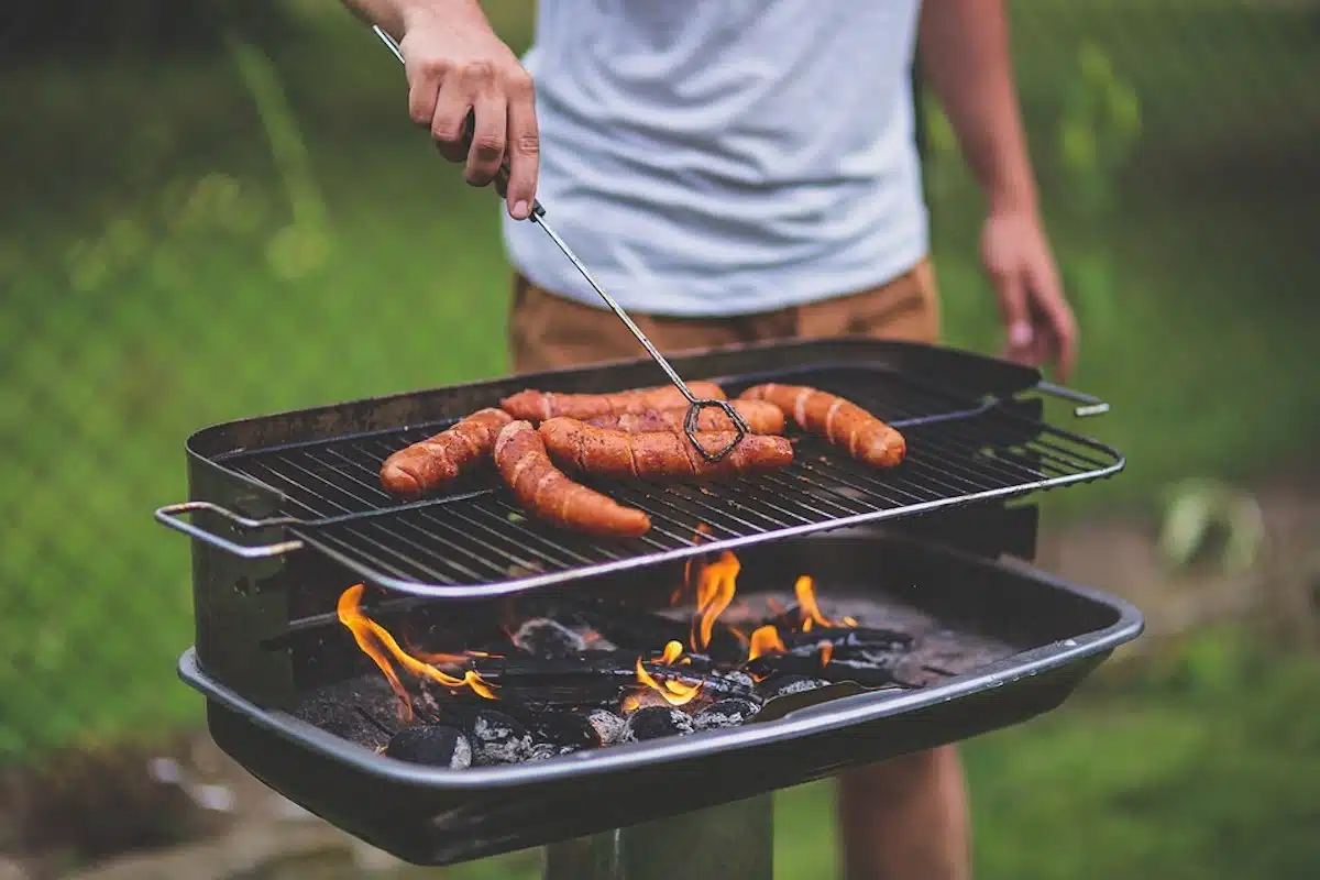 Homme avec une pince derrière son barbecue et saucisses